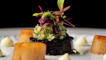 Un plato con base oscura, cubierto de una mezcla colorida de verduras y adornado con hojas verdes y púrpuras.