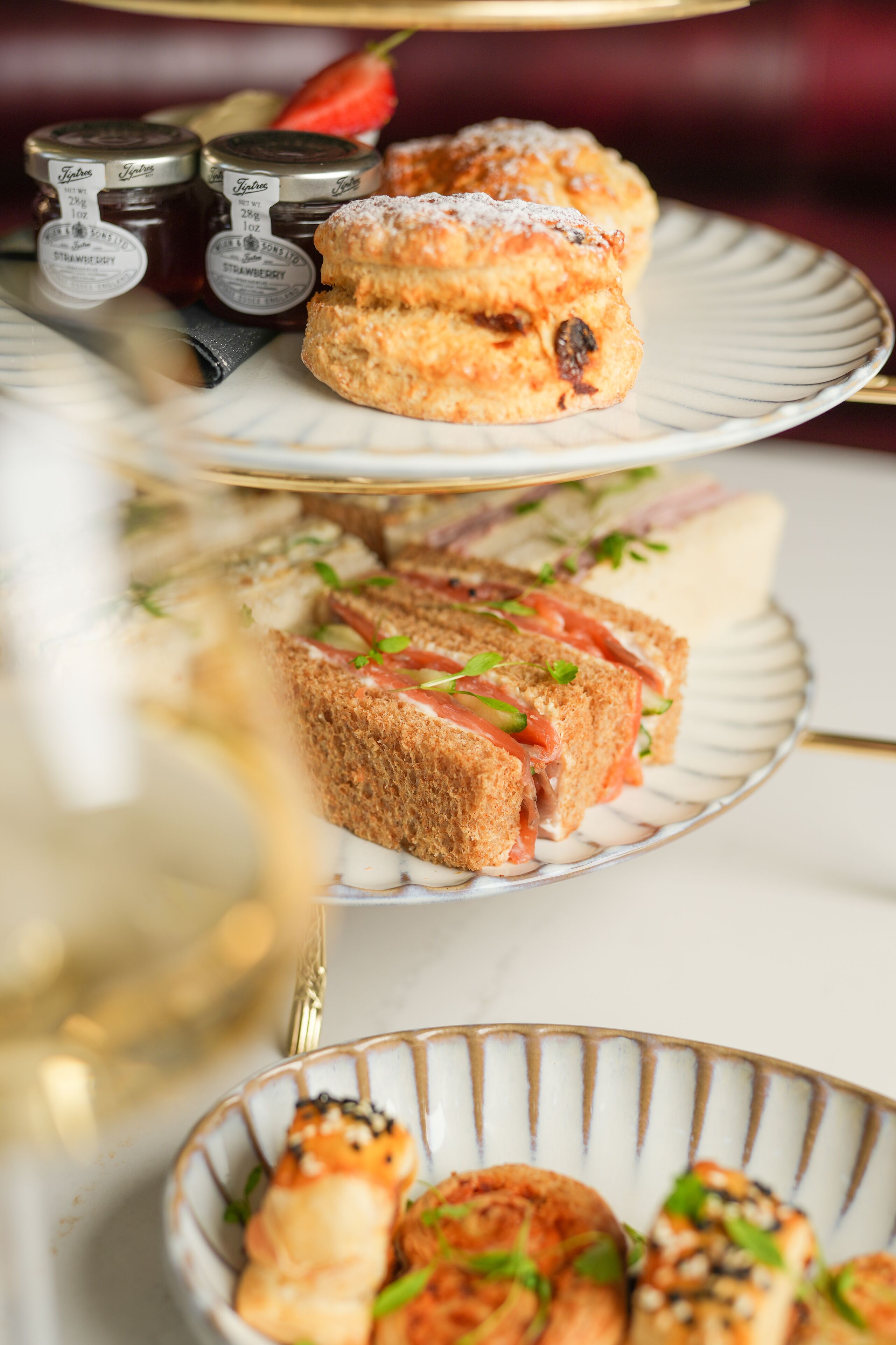 Une table avec trois assiettes de nourriture, comprenant des scones, des sandwichs et des crevettes.