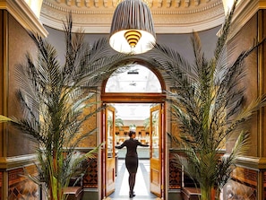 Un lobby imponente con un arco central, palmeras grandes y un candelabro.