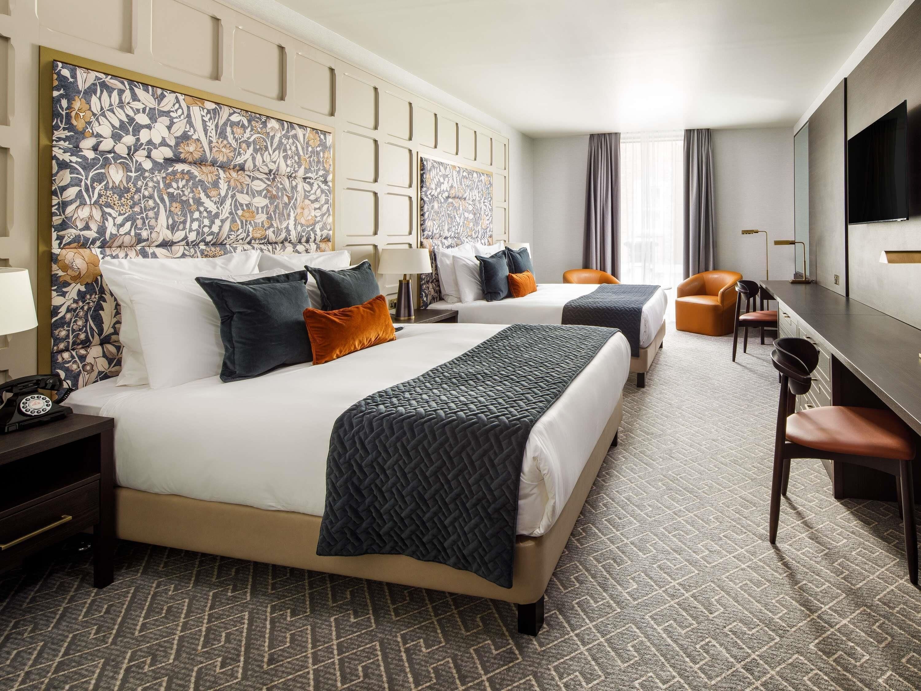 A hotel room with two beds, a desk, a chair, a TV, and a patterned carpet.