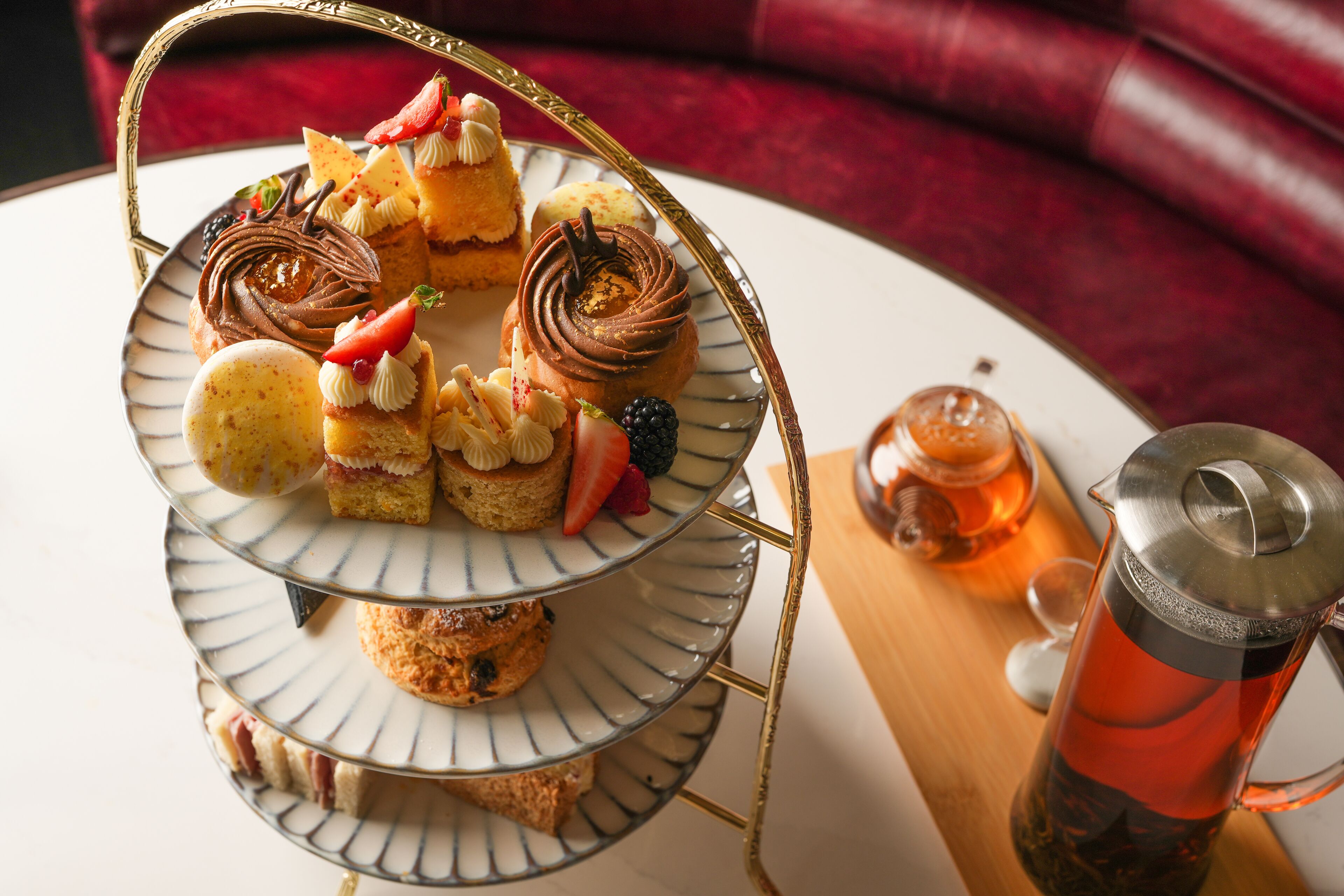 A three-tiered dessert stand with various pastries and a teapot on a table.