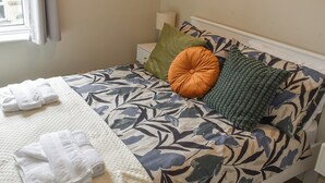 Un letto rifatto con cura, con una coperta a motivi floreali, una coperta bianca e diversi cuscini, tra cui uno verde e uno arancione.