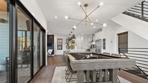 Une cuisine moderne dotée d’un îlot central, d’un coin repas avec table de billard et d’un escalier avec une rampe noire.