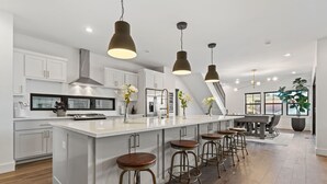 Une cuisine moderne dotée d’un grand îlot central, de tabourets de bar, de luminaires suspendus et offrant une vue sur l’extérieur.