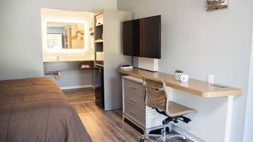 A bedroom with a bed, a desk with a chair, a television, and a wardrobe.