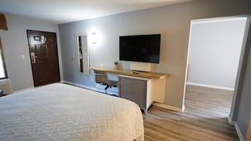 A bedroom with a large bed, a desk with a flat-screen TV, a chair, and a wardrobe.
