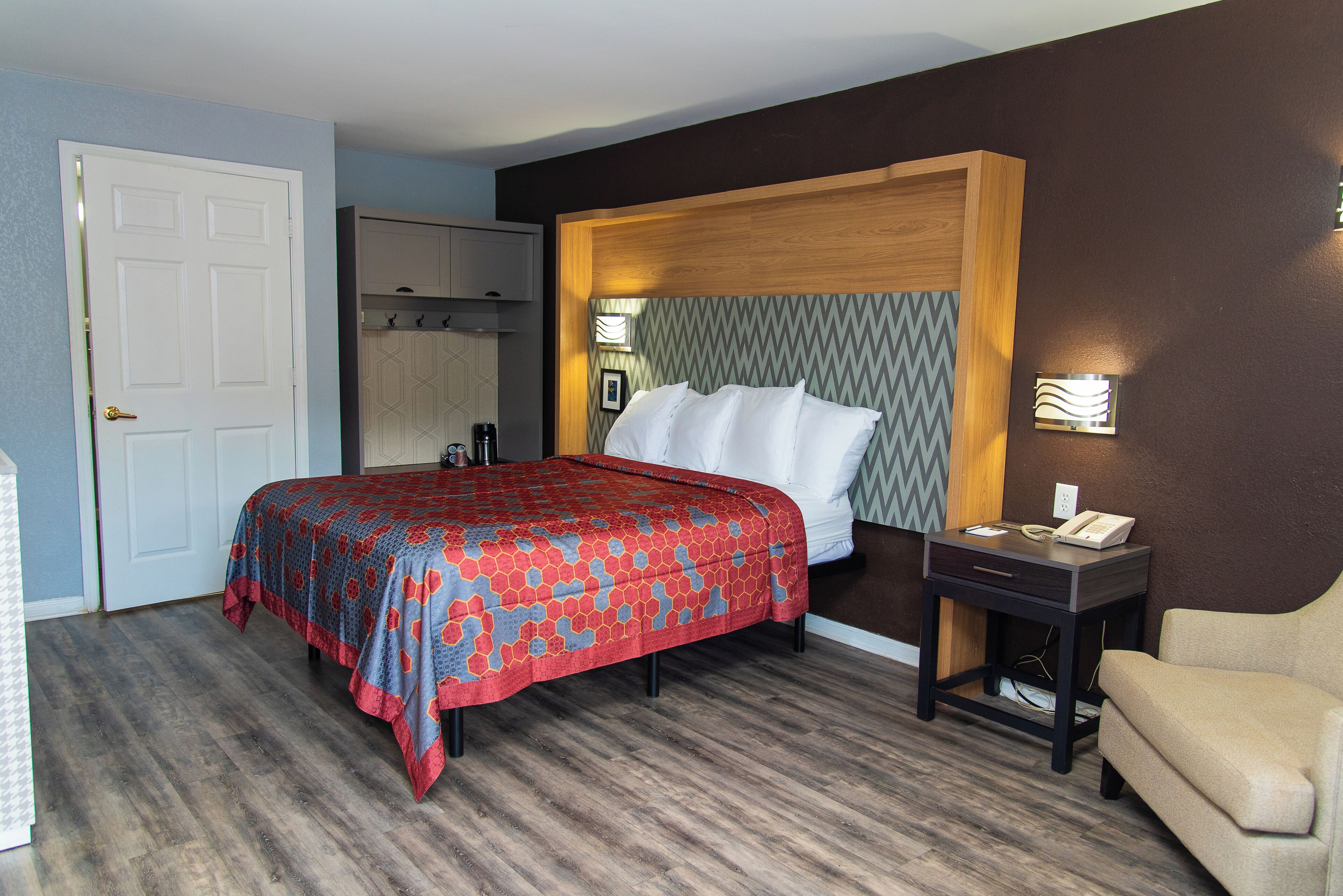 A hotel room with a bed, a bedside table with a phone, a chair, a wardrobe, and a mirror.
