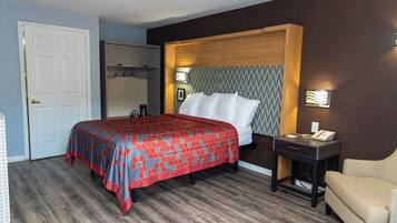 A hotel room with a bed, a bedside table with a phone, a chair, a wardrobe, and a mirror.