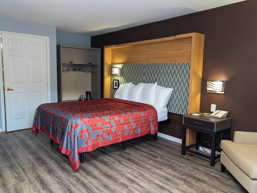 A hotel room with a bed, a bedside table with a phone, a chair, a wardrobe, and a mirror.