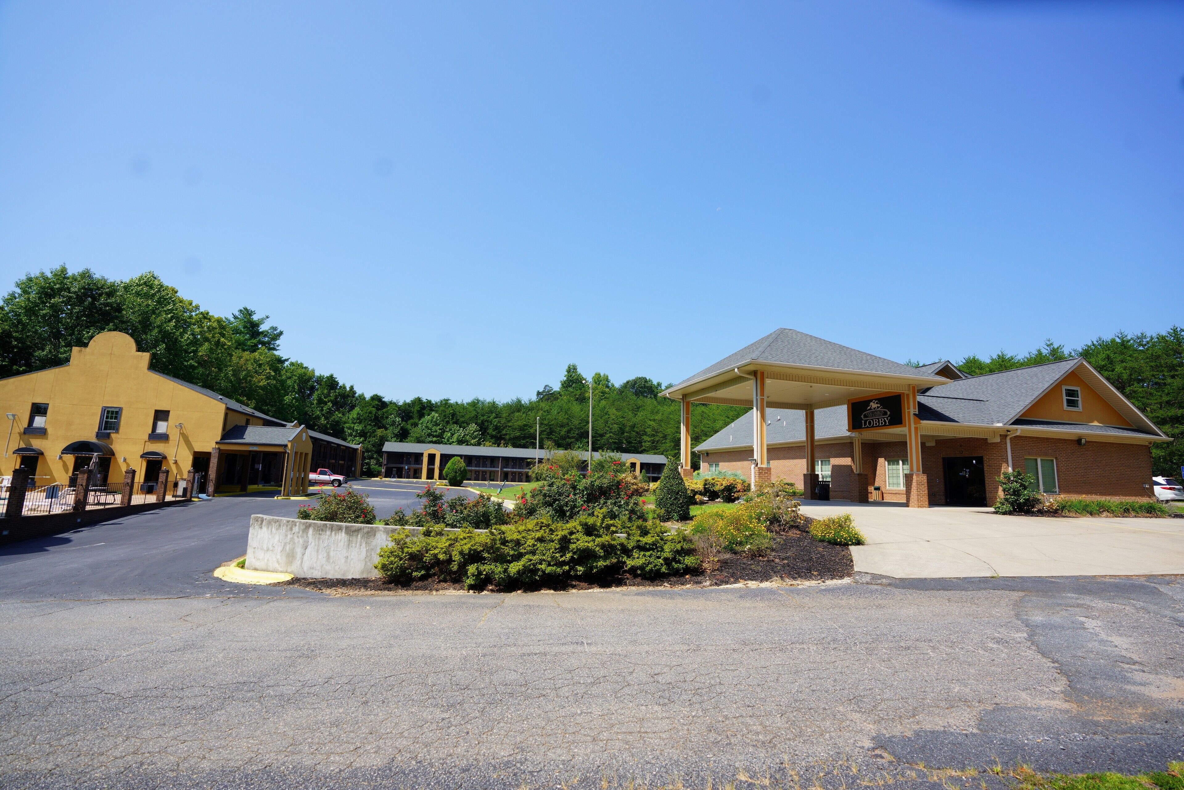 A hotel with a covered lobby, a parking lot, and a building with a yellow facade.