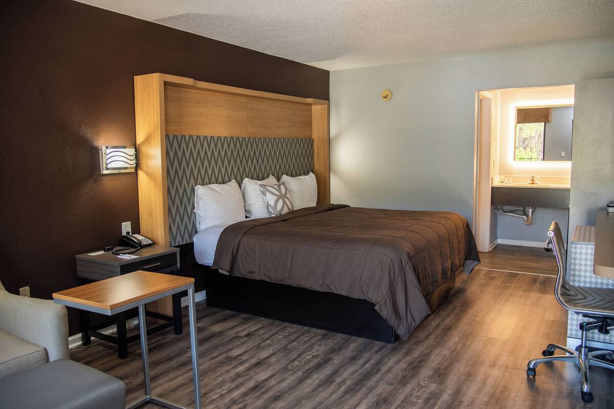 A hotel room with a bed, bedside table, chair, desk, and a small table.