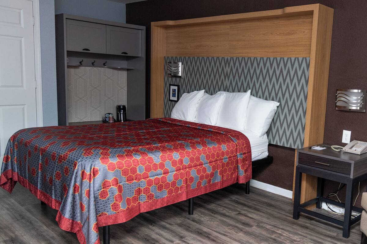 A bedroom with a bed, a bedside table, a wardrobe, and a wall-mounted light fixture.