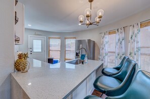 Modern kitchen with central island, oven, and refrigerator, complemented by a seating area with two chairs.