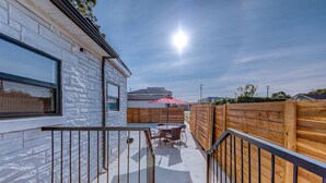 Une terrasse extérieure couverte, dotée d’une plateforme en bois, d’une table et de chaises, ainsi que d’un parasol rouge.