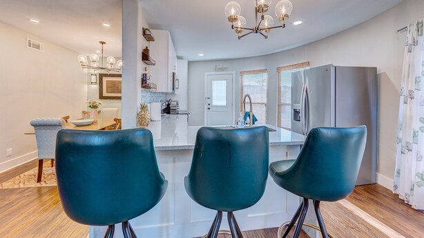 Une cuisine moderne dotée d’un îlot central, d’un coin repas avec des chaises de couleur turquoise et d’un lustre.