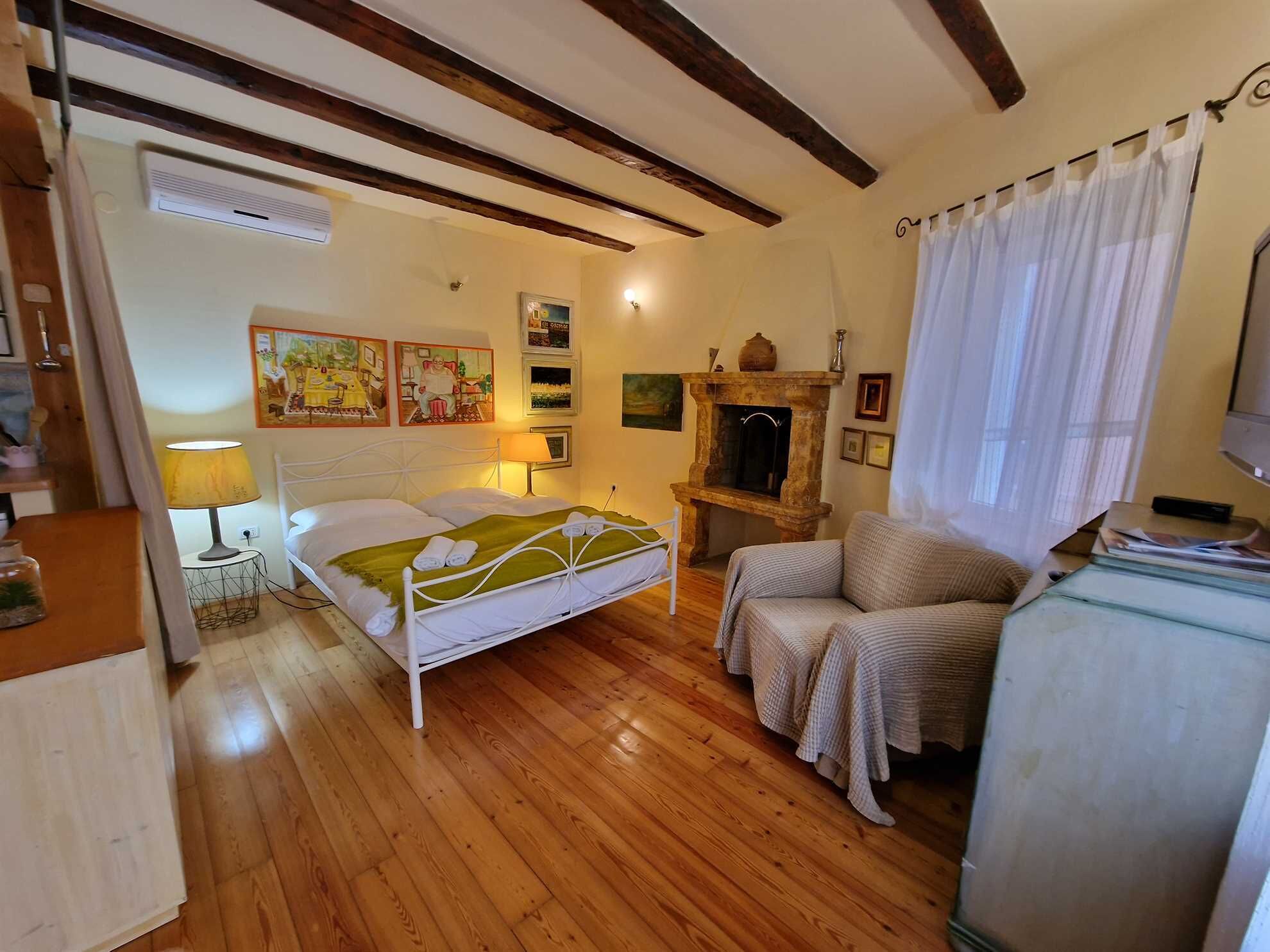 Ein gemütliches Schlafzimmer mit Holzboden, einem Bett mit weißer Bettwäsche, einem kleinen Tisch mit Lampe, einem Sessel und einem Kamin.