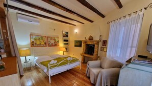 Una camera accogliente con pavimento in legno, un letto con biancheria bianca, un tavolino con una lampada, una sedia e un camino.