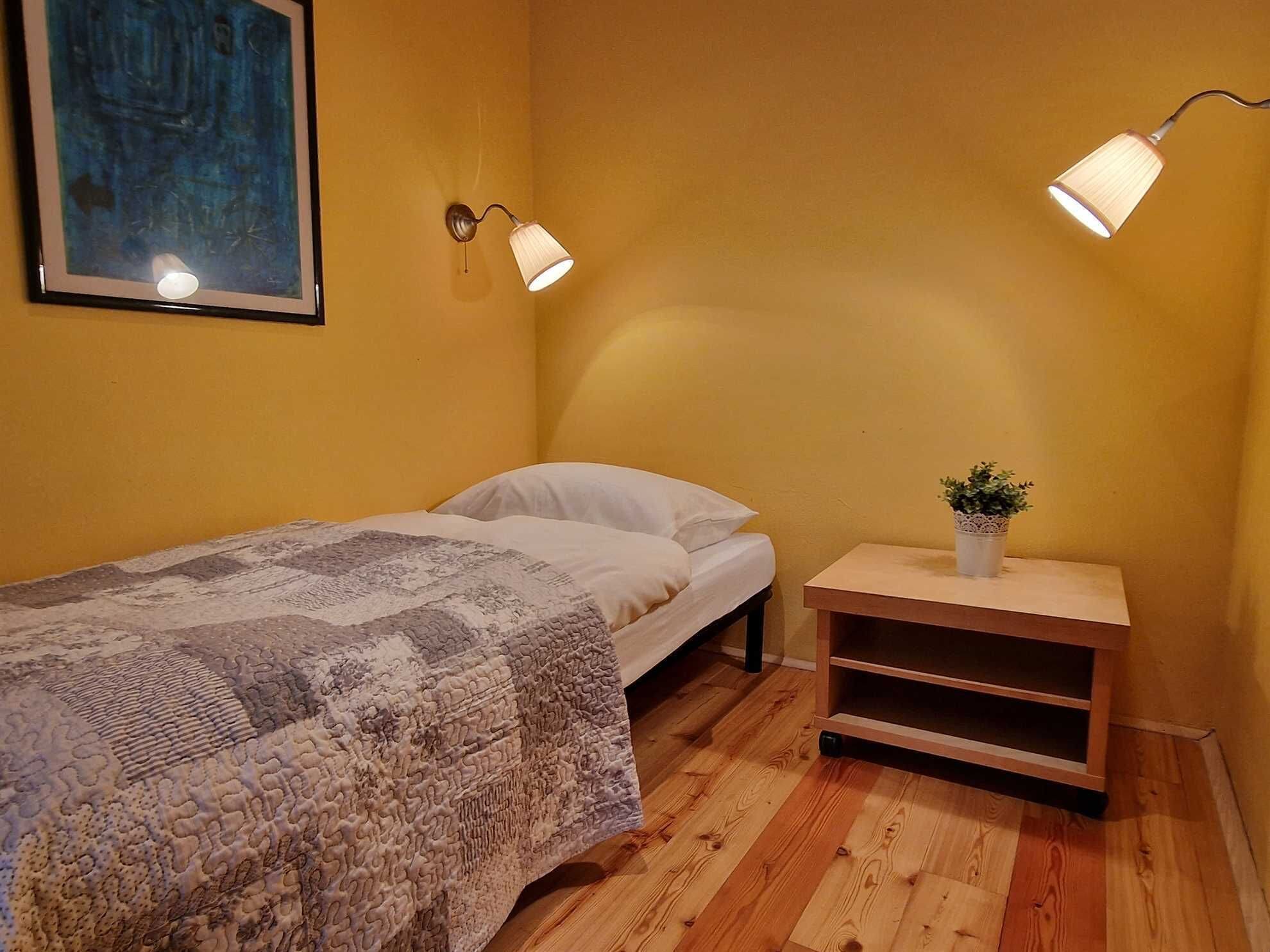 A small, cozy bedroom with a single bed, a nightstand with a plant, and two wall-mounted lamps.