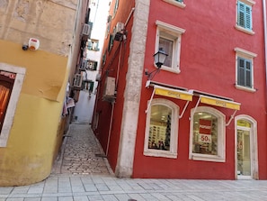 A narrow cobblestone street with a red building featuring an 'Office Shoes' shop with a 50% discount sign. - ARTISTICO - Studio Apartment (Rovinj)
