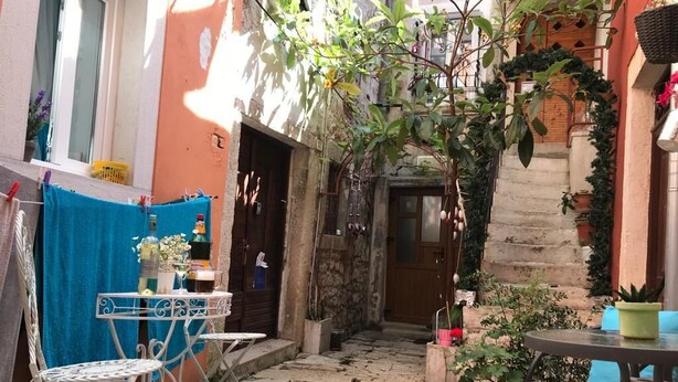A narrow stone-paved courtyard with a small table and chairs, a door, and potted plants. - LIMONA - Studio Apartment (Rovinj)