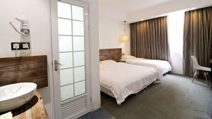 Quarto de hotel com cama, mesa de cabeceira, cadeira, banheiro com pia e janela com cortinas.