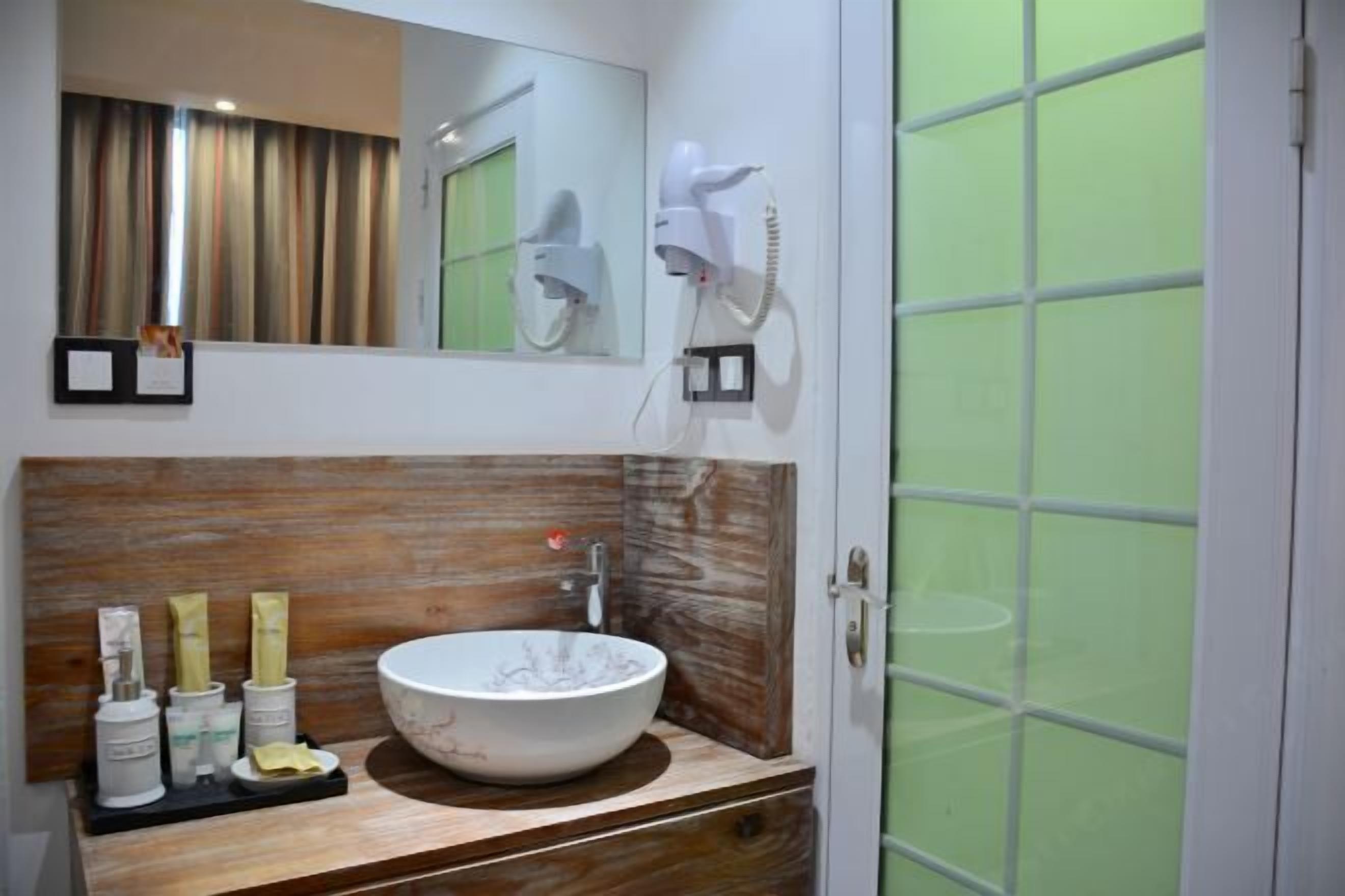 Un baño con tocador de madera, un lavamanos blanco grande y un espejo encima. Hay dos secadores de pelo montados en la pared.