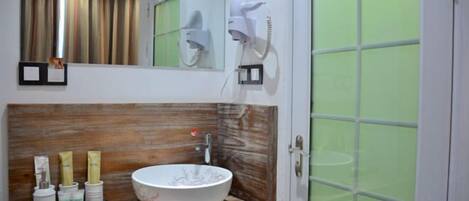 Une salle de bain avec un meuble-lavabo en bois, un grand lavabo blanc et un miroir au-dessus. Deux sèche-cheveux sont fixés au mur.