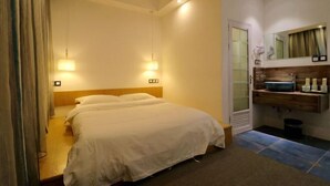 Quarto de hotel com cama, luminárias de cabeceira, espelho, prateleira de madeira com produtos de higiene pessoal e porta para um banheiro.