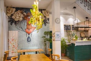 A restaurant interior with a mural, wooden tables, and a green counter. - Xiyu Hostel · Cat Café (Yangshuo)