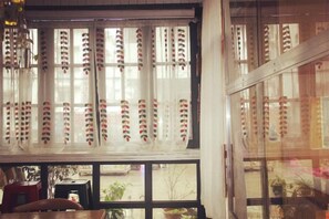 A room with a large window featuring a decorative curtain with a pattern of red and white elements. - Xiyu Hostel · Cat Café (Yangshuo)