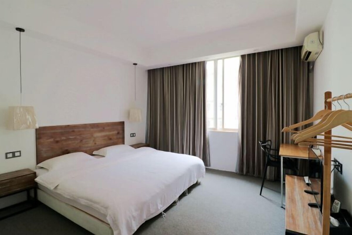 Habitación de hotel con cama, escritorio, silla, lámpara colgante y ventana con cortinas.