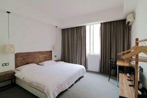 Habitación de hotel con cama, escritorio, silla, lámpara colgante y ventana con cortinas.