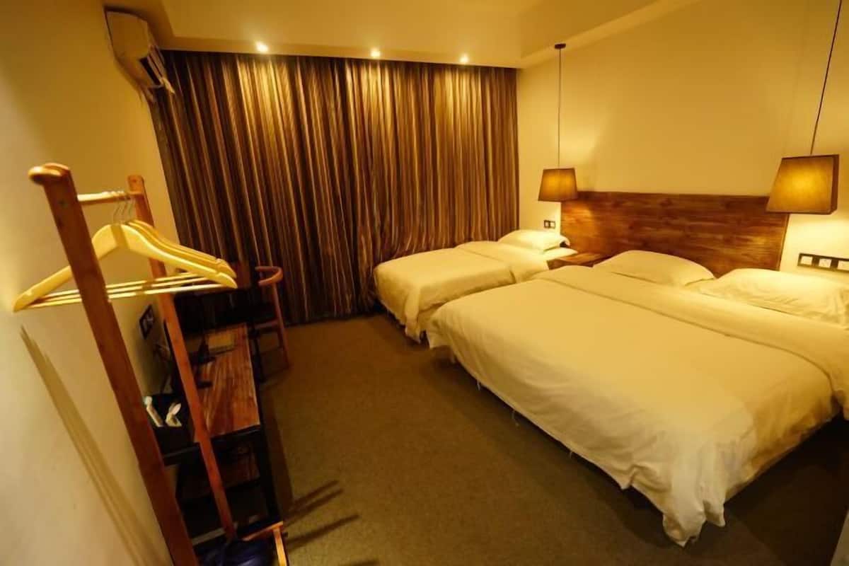 A hotel room with two beds, a wooden chair, a coat rack, and a curtain.