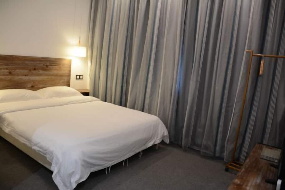 A hotel room with a wooden headboard, a bed with white linens, a nightstand with a lamp, and a window with striped curtains.