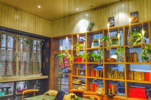 A room with a wooden bookshelf, hanging plants, and a window with curtains. - Xiyu Hostel · Cat Café (Yangshuo)