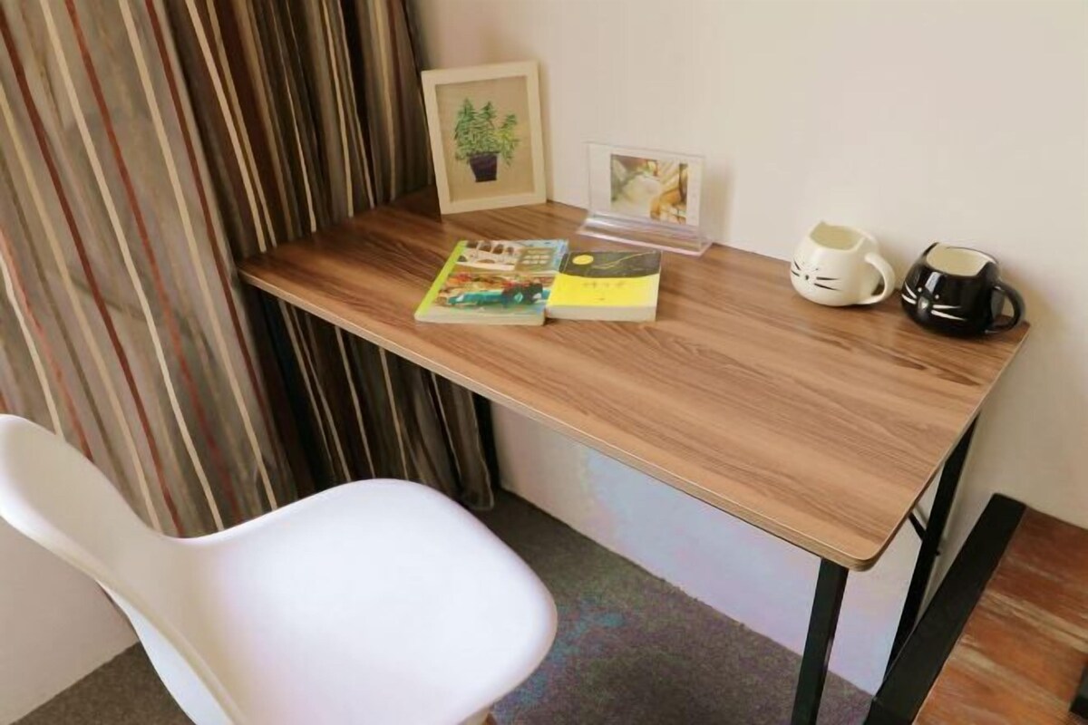Un escritorio de madera con una silla blanca, un cuadro enmarcado de una planta, un libro, una taza de café y una mug.