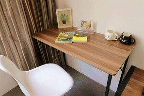 A wooden desk with a white chair, a framed picture of a plant, a book, a coffee cup, and a mug. - Xiyu Hostel · Cat Café (Yangshuo)