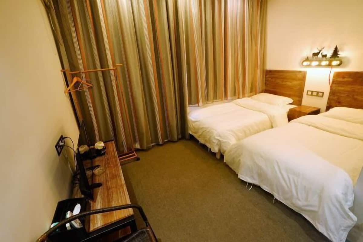 A hotel room with two beds, a wooden desk, and a headboard with a light fixture.