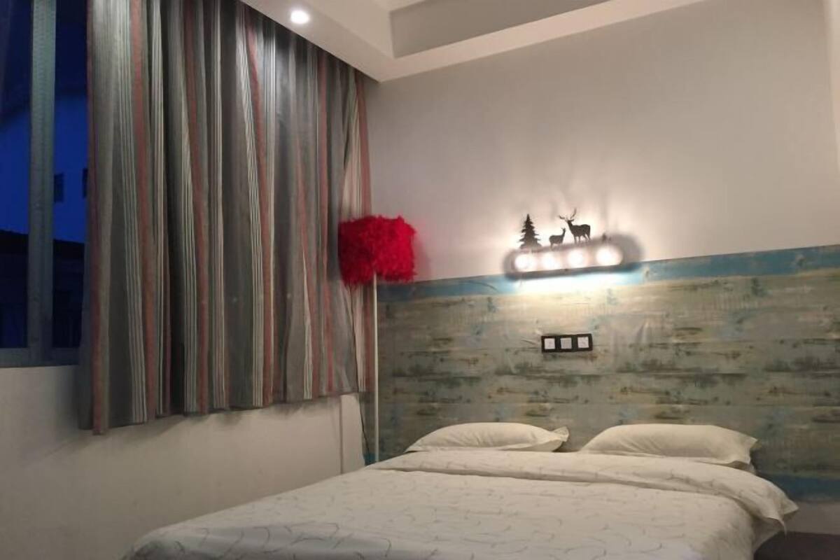 A bedroom with a bed, striped curtains, a red decorative item, and a wall-mounted light fixture.