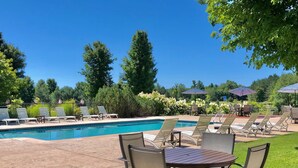 A pool area with lounge chairs and a table, surrounded by greenery and trees. - Cottage 7 sleeps 6 people (Empire)