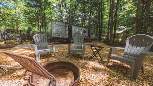 A campsite with a fire pit, two Adirondack chairs, and a portable RV. - RV Rental #6 Sleeps 6 people (Empire)