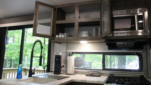 A compact kitchen with a built-in microwave, a gas stove, and a window with blinds. - RV Rental #6 Sleeps 6 people (Empire)