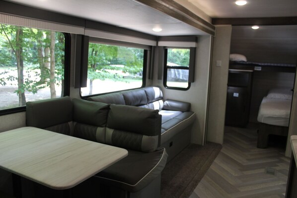 A compact RV interior with a dining area, seating, and a sleeping berth.