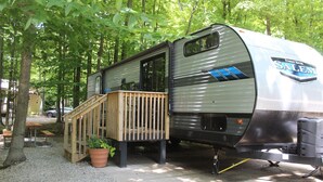 A mobile home with a wooden deck and a ramp, surrounded by trees. - RV Rental #15 Sleeps 6 people (Empire)