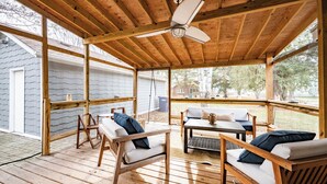 A wooden deck with a ceiling fan, outdoor seating, and a view of a house and trees.