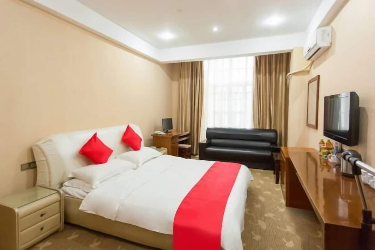 Ein Hotelzimmer mit Bett, Schreibtisch, Fernseher und einem Fenster mit Vorhängen.