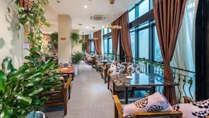 Un restaurant spacieux avec de longues tables, des chaises en bois et de grandes fenêtres ornées de rideaux.