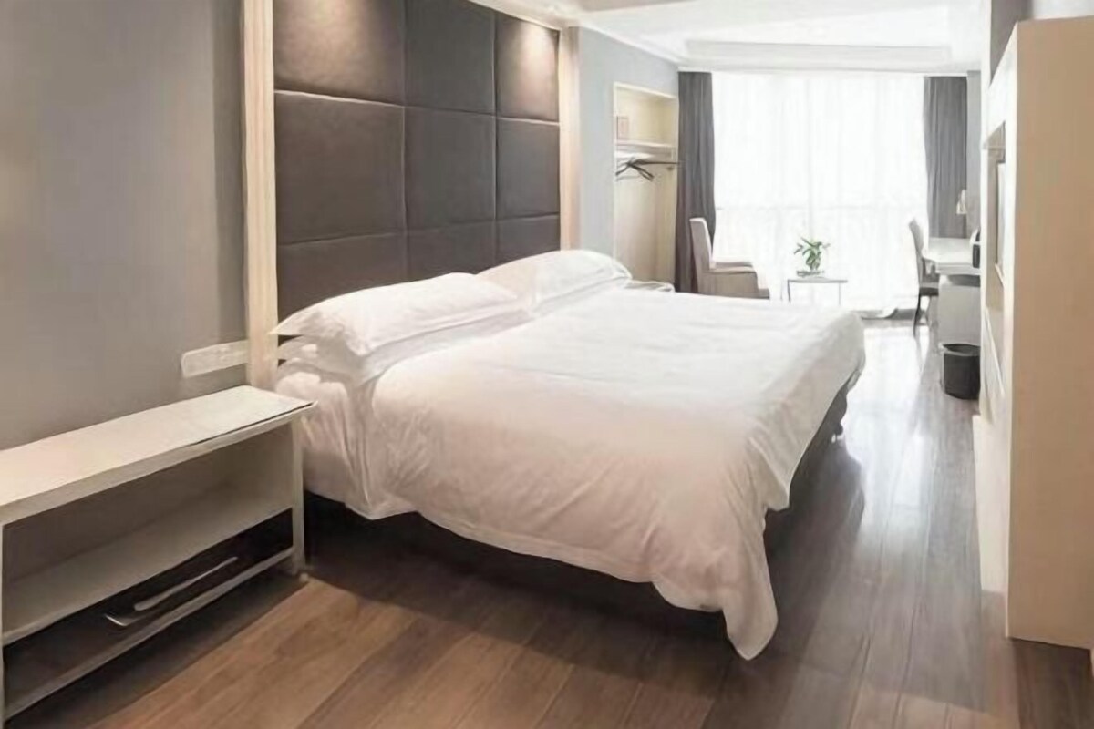 A modern hotel room with a large bed, a bedside table, a small desk, and a chair.