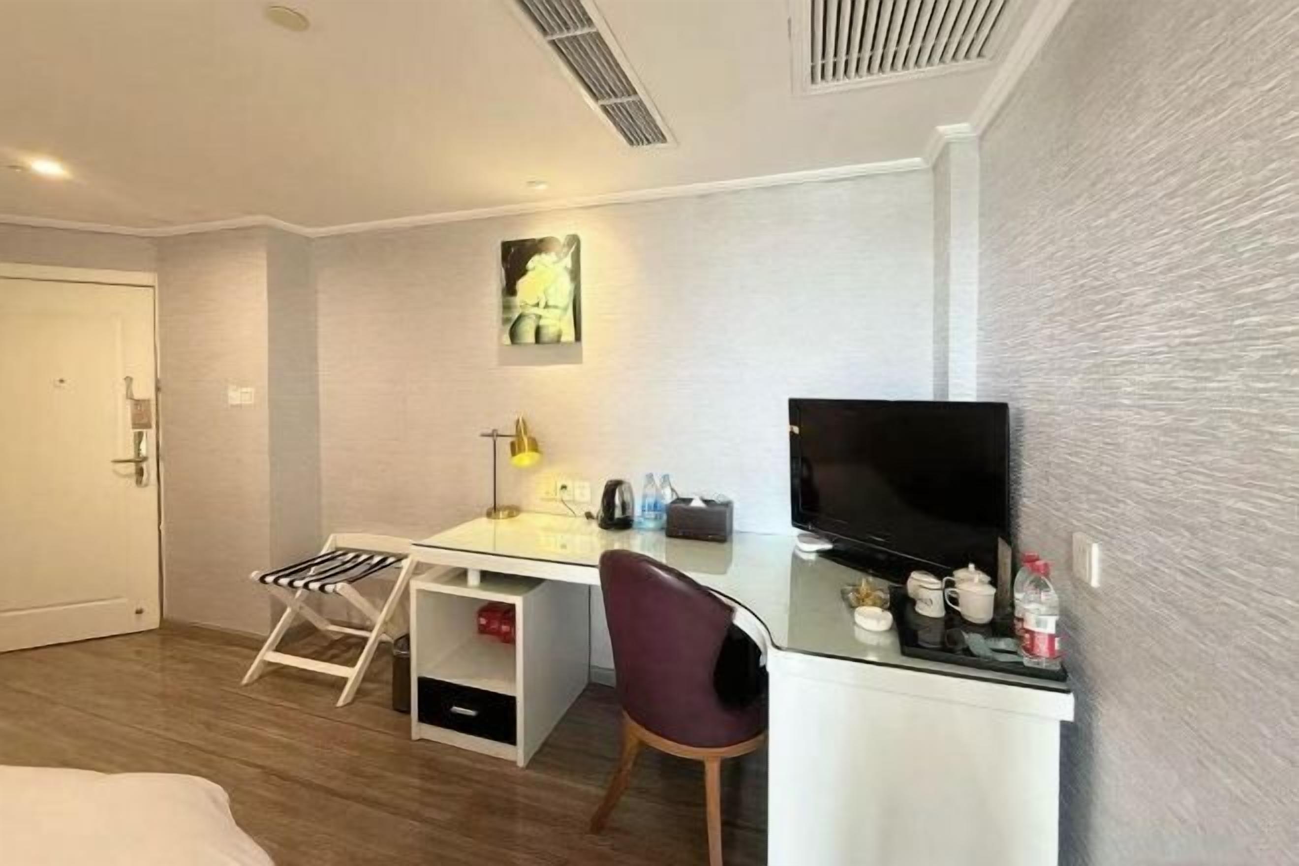 Una habitación de hotel con una cama, un escritorio con una silla, un televisor y un cuadro en la pared.