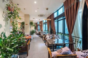 A restaurant with indoor seating, large windows, and hanging plants.